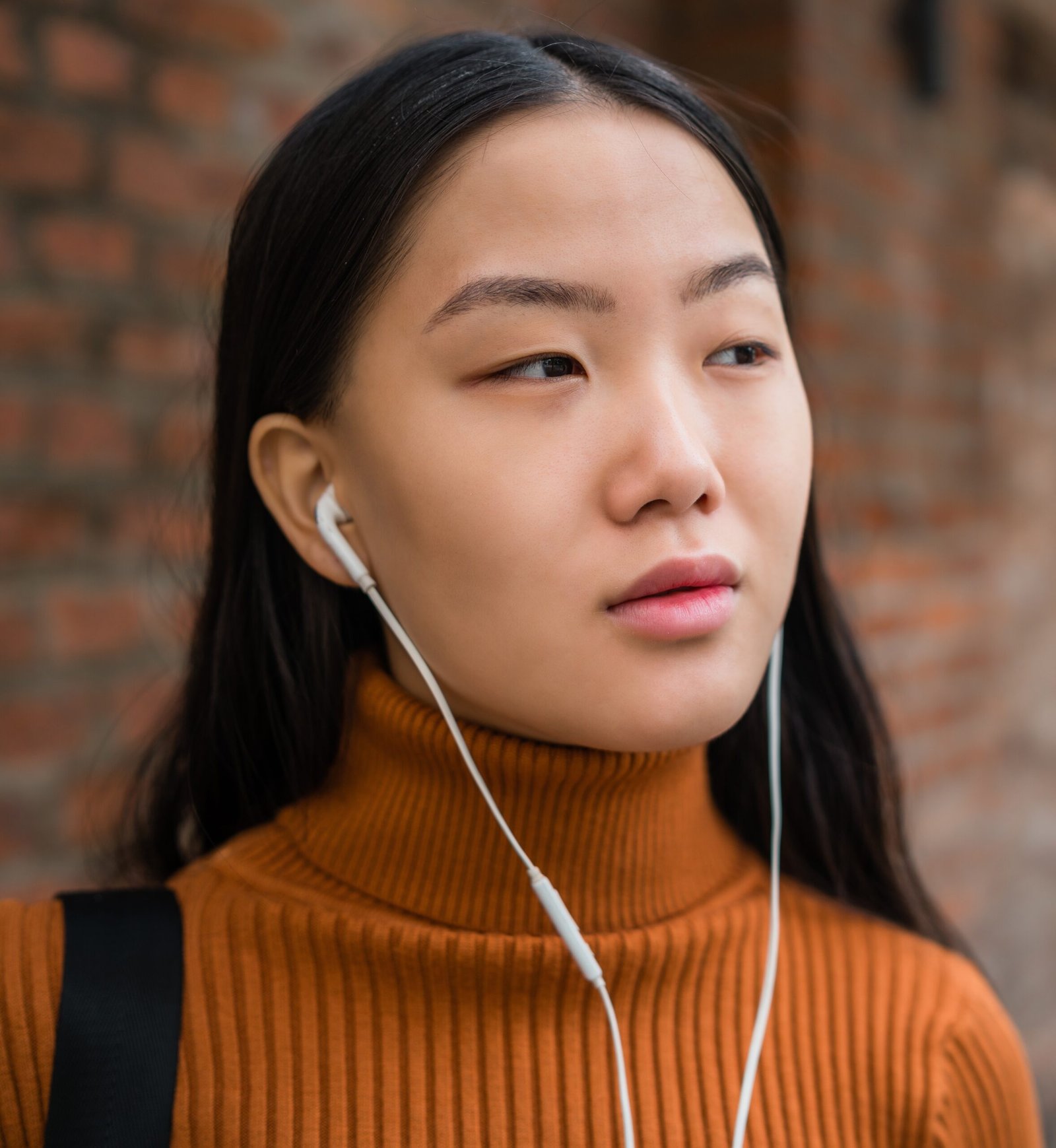 Portrait of young Asian woman listening to music with earphones in the street. Outdoors.